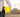 A surveyor holding a yellow protective helmet in a hand with a construction site in the background.