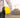 A surveyor holding a yellow protective helmet in a hand with a construction site in the background.
